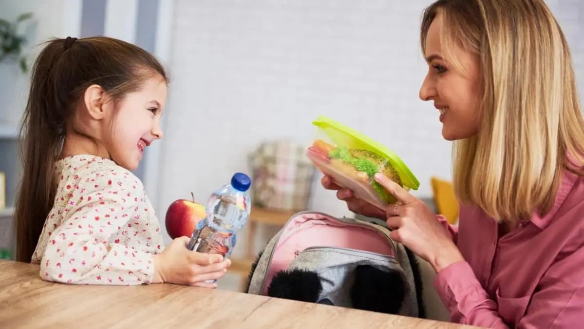 maminka dceři dává do batohu svačinu do školy