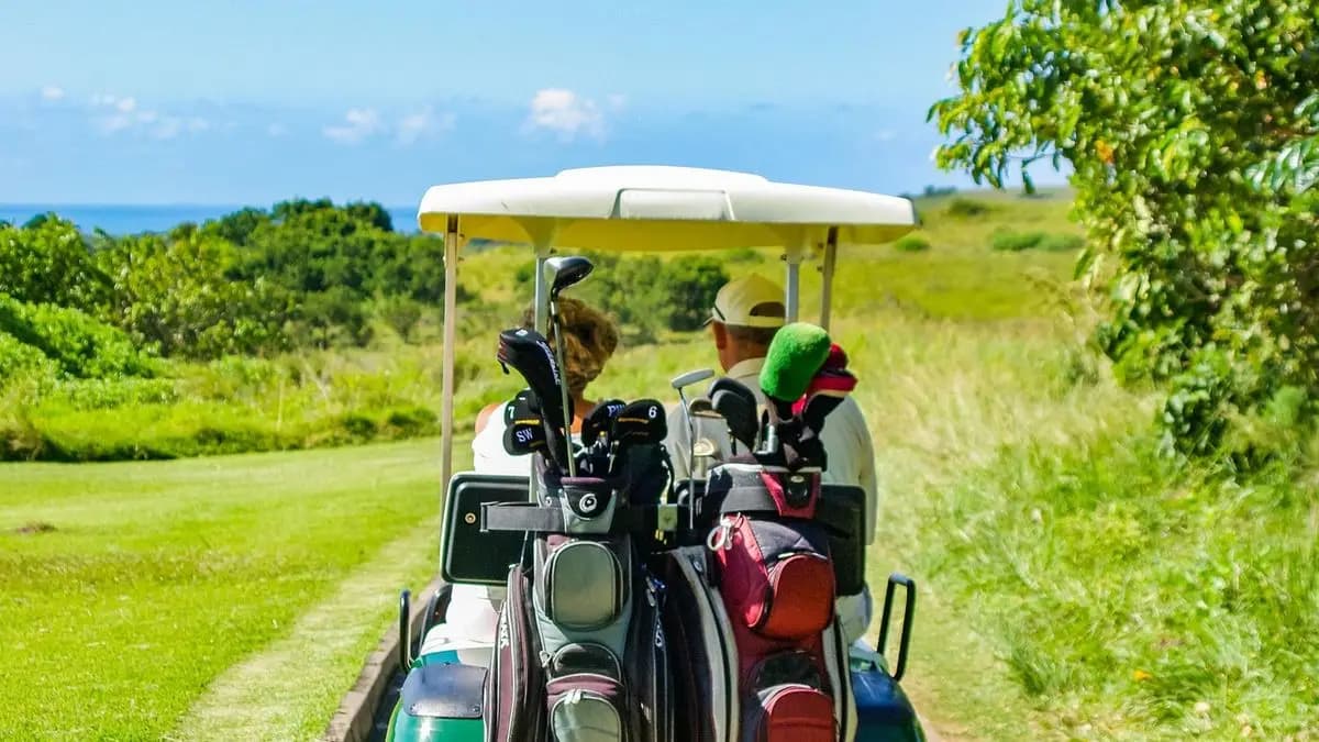 dva lidé jedou po golfovém hřišti ve vozíku