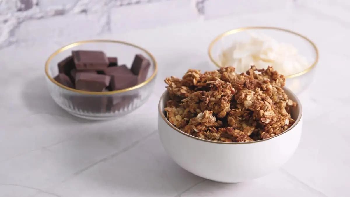 granola v misce, za ní mističky s čokoládou a kokosem