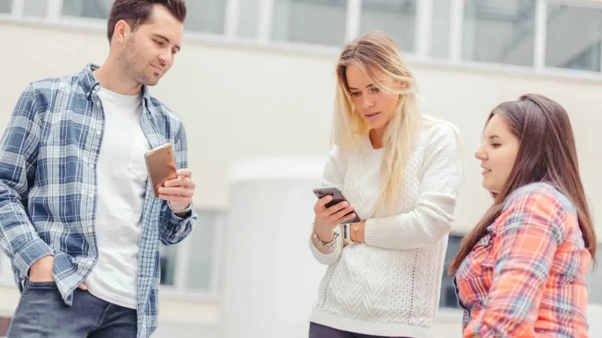 Tři mladí lidé stojí venku a čtou zprávy v mobilech