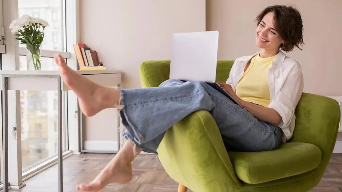 Žena sedí shrbeně v zeleném křesle s notebookem na kolenou