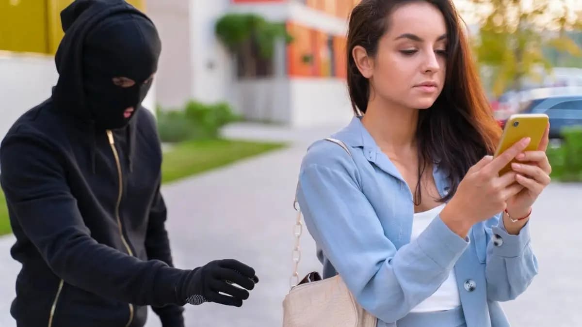 Žena se dívá do mobilu, zezadu k její kabelce sahá muž v kukle. Žena se dívá do mobilu, zezadu k její kabelce sahá muž v kukle.