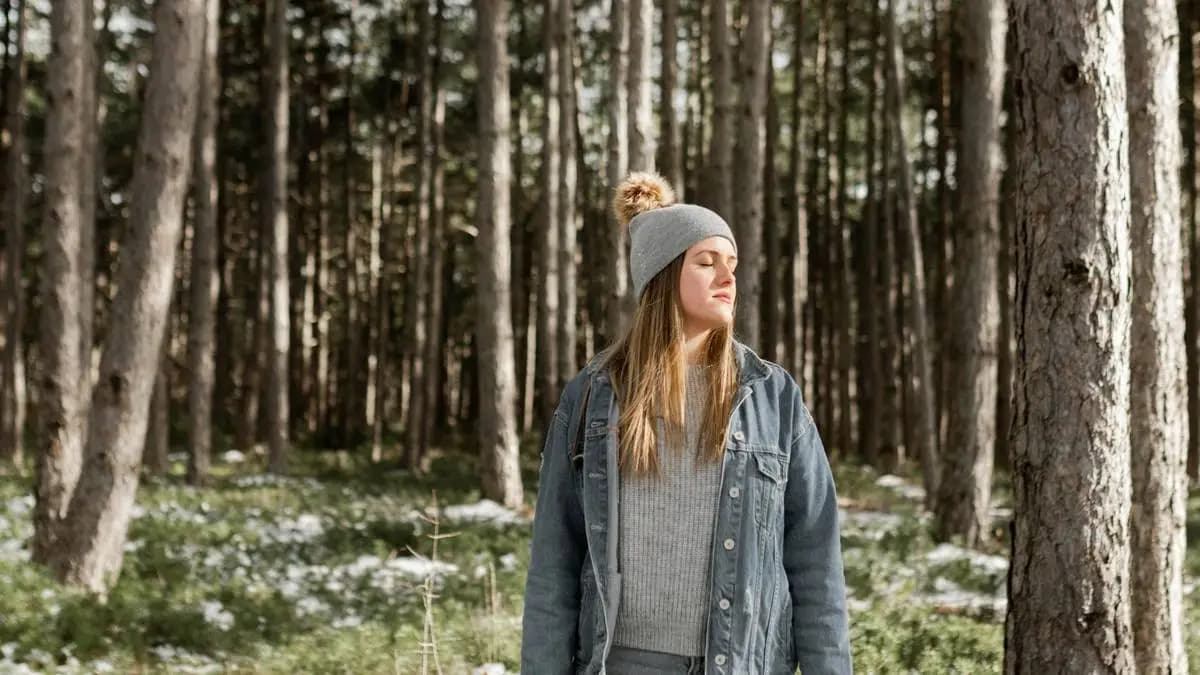 Mladá žena se zavřenýma očima stojí v lese mezi vysokými stromy Mladá žena se zavřenýma očima stojí v lese mezi vysokými stromy