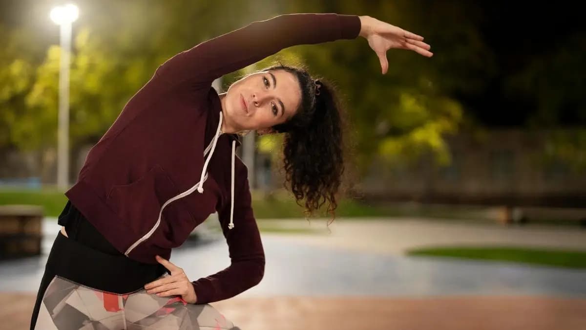 Žena se večer protahuje v parku pod pouliční lampou Žena se večer protahuje v parku pod pouliční lampou