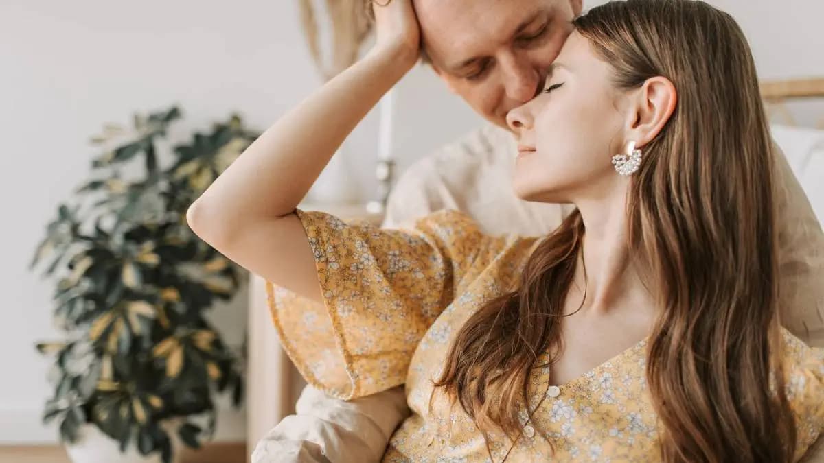 pár doma, žena vjíždí prsty do vlasů partnera, který sedí za ní pár doma, žena vjíždí prsty do vlasů partnera, který sedí za ní