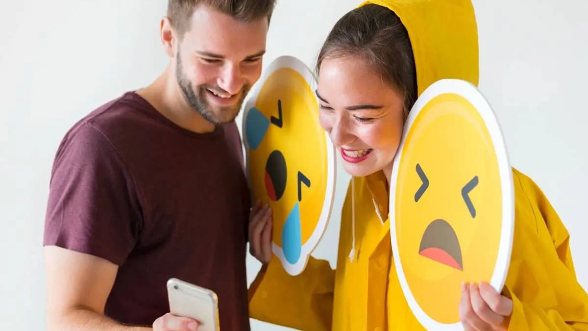Usměvavá dvojice s mobilem a velkými cedulemi smutných emoji. Usměvavá dvojice s mobilem a velkými cedulemi smutných emoji.
