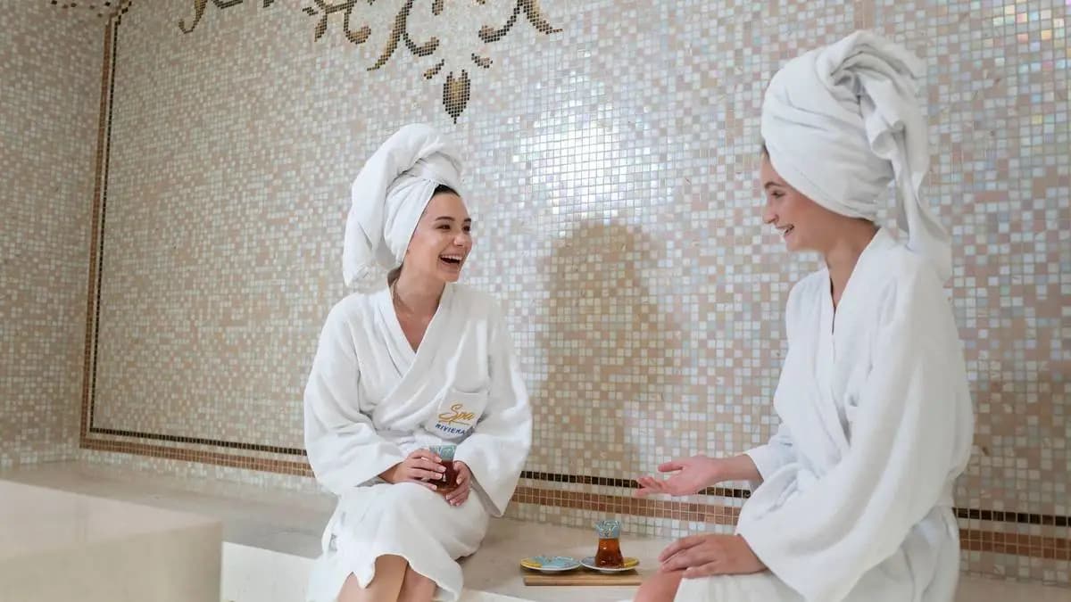Dvě ženy v županech a s ručníky na hlavě pijí čaj ve wellness. Dvě ženy v županech a s ručníky na hlavě pijí čaj ve wellness.